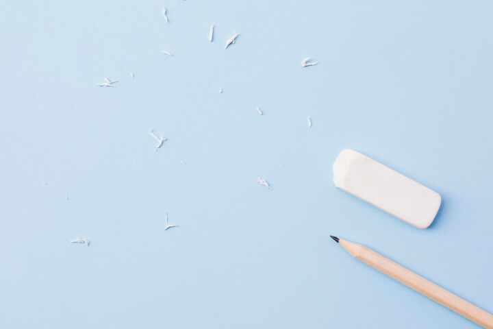 A pencil and eraser lying next to each other on a piece of paper with recently erased marks.
